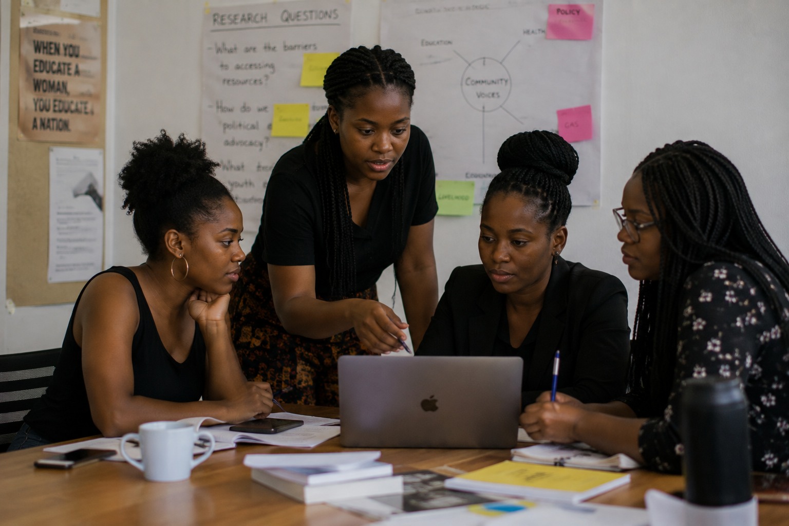 A woman standing over a laptop explaining something to three women seated around a table